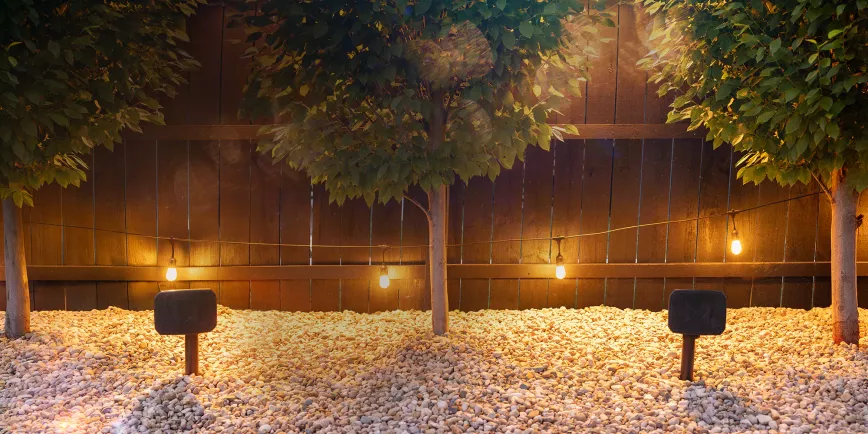 klipsch_courtyard_speakers_outdoors_in_gravel_between_symmetrical_trees_2_2000x1000.webp